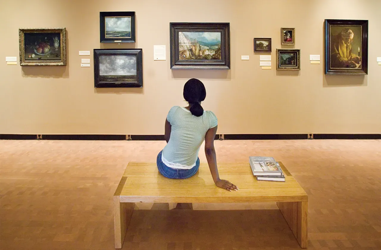 Student sitting on a bench looking at paintings on the wall of the museum